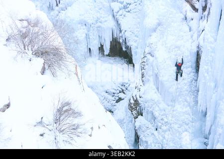 Eiskletterer besteigt den gefrorenen Wasserfall in der Winterschlucht Stockfoto