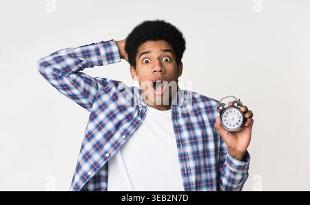 Schockierter Kerl, der den Wecker über hellem Hintergrund hält Stockfoto