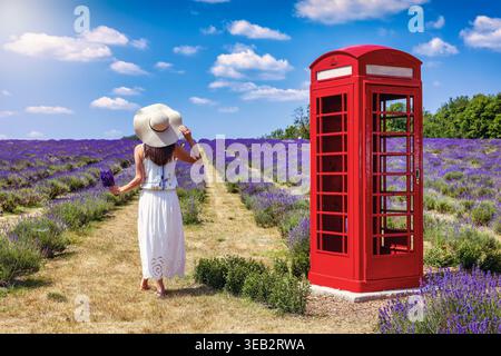 Eine Frau in einem weißen Sommerkleid steht in voller Blüte auf einem Lavender-Feld neben einer klassischen britischen Telefonzelle Stockfoto