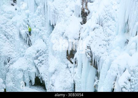 Eiskletterer besteigt den gefrorenen Wasserfall in der Winterlandschaft Stockfoto