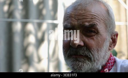 Porträt eines älteren verzweifelten ukrainischen Mannes im Sommergarten. Ein älterer, trauriger bärtiger Mann, der ein besticktes Hemd trägt und draußen in die Kamera schaut. Reif Stockfoto
