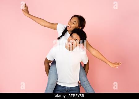 Zwei junge Individuen posieren fröhlich vor rosafarbenem Hintergrund während eines spielerischen Moments Stockfoto