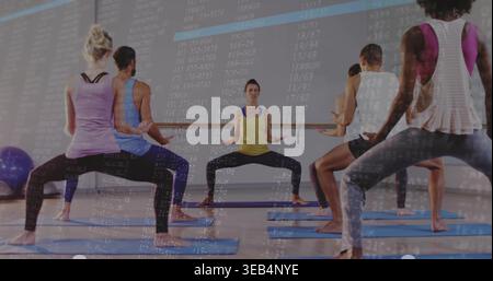 Führender Trainer, der in der Hocke im Studio sitzt, in gelben, dunklen Leggings mit blauen Matten-Code-Overlay Stockfoto