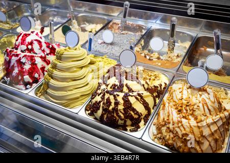 Nahaufnahme einer lebendigen Vitrine in einer modernen Gelateria, die eine Auswahl köstlicher Gourmet-Eissorten mit Belag präsentiert, die den Kunden an einem warmen Sommertag zur Verfügung stehen Stockfoto