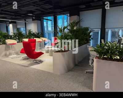 Moderner Büro-Lounge-Bereich mit roten Stühlen, Tischen und Pflanzen im Innenbereich mit offenem Arbeitsbereich und großen Fenstern. Business-Umgebung, Business-Spa Stockfoto
