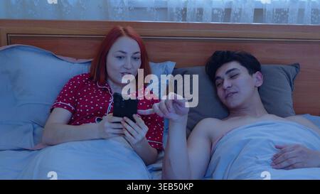 Pärchen im Bett mit Handys vor dem Schlafen Stockfoto