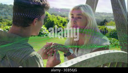 Hände halten, Paar auf Schaukel auf der Wiese, Mann grünes Hemd, Frau weiße Bluse, digitales Netz, Uhr Stockfoto