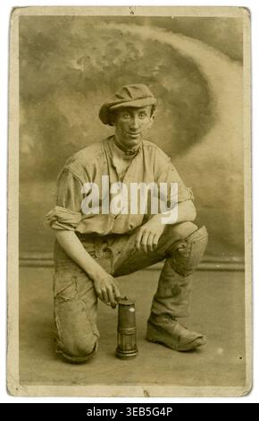 Postkarte aus den 1900er Jahren eines jungen Bergarbeiters mit flacher Kappe, Lampe, mit mobilem Studio-Hintergrund, von J Roberts, Leeds. Yorkshire, Großbritannien, um 1920 Stockfoto