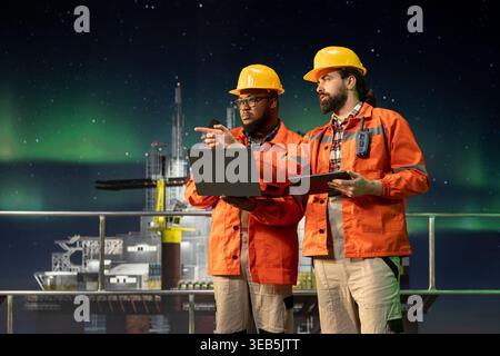 Offshore-Plattform-Engineering-Team mit Laptop zur Fernsteuerung von Unterwassersystemen bei Nacht. Professionelle Überwachung der Anomalie-Erkennung mit Notizbuch auf Bohrderrick Stockfoto