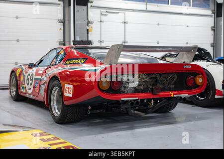 Dreiviertelansicht eines roten Ferrari 512 BB LM historischen Rennwagens mit GT2-Lackierung und einem großen Heckspoiler, der in einer professionellen Boxengarage geparkt ist. Stockfoto
