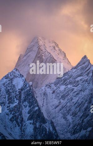 Blick auf die schneebedeckten Haldi-Kegel-Berggipfel unter einem weichen rosa und orangen Sonnenuntergangshimmel mit hellen Wolken in Khaplu, Baltistan, Pakistan. Stockfoto