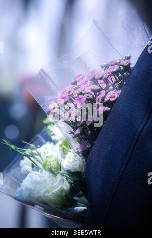 Blick auf eine Person, die Sträuße mit rosa Chrysanthemen und weißen Rosen in klarem Plastik trägt. Stockfoto