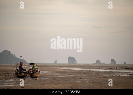 Krabi Thailand 19. Februar 2026. Zwei Fischerboote sitzen bei Ebbe an der exponierten matschigen Küste mit Inseln in der Ferne. Stockfoto