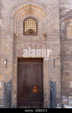 Blick auf die Moschee von al-Salih Tala'i mit einer großen Holztür, komplizierten Steinschnitzereien und einem kleinen bogenförmigen Fenster Kairo, Ägypten. Stockfoto