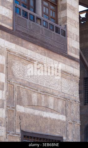 Blick auf die komplizierte arabische Kalligraphie und Steinschnitzereien an der Fassade des Al Ghuri Dome Komplexes mit einem traditionellen Holzbalkon in Kairo, Ego Stockfoto