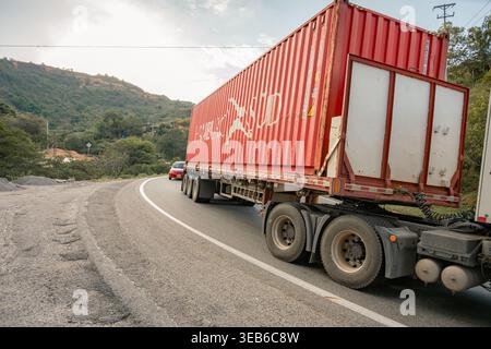 Jordanien, kolumbien - agosto 30, 2025 Red Container Truck, der Fracht auf einer gewundenen Asphaltstraße transportiert und Logistik und Handel durch ein malerisches n Stockfoto
