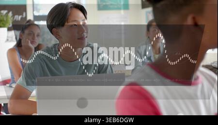 Beobachten Sie den männlichen Jugendlichen asiatischen Schüler, der sich im Klassenzimmer mit einem Laptop mit Waveform-HUD fokussiert Stockfoto