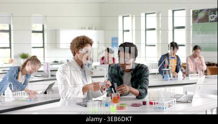 Transfer von flüssigen Schülern in Laborkittel und Brille im Schullabor mit Becher, Reagenzgläsern Stockfoto