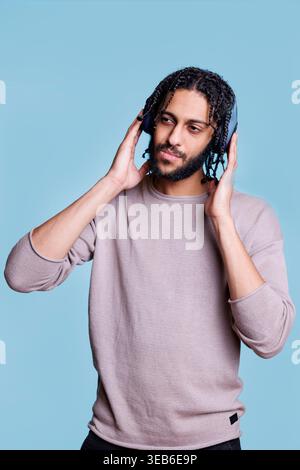 Arabischer Mann, der Lieder hört, kabellose Kopfhörer auf dem Kopf berührt und mit nachdenklichem Gesichtsausdruck wegschaut. Person in Ohrhörern, die legere Kleidung trägt und Musik genießt Stockfoto