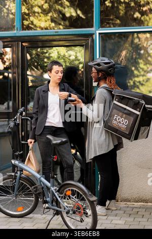 Büroangestellter bezahlt die Lieferung mit einer kontaktlosen Zahlungstransaktion für die Smartwatch. Ein afroamerikanischer Kurier hält Pos Terminal, steht in der Nähe des Firmengebäudes im Freien Stockfoto