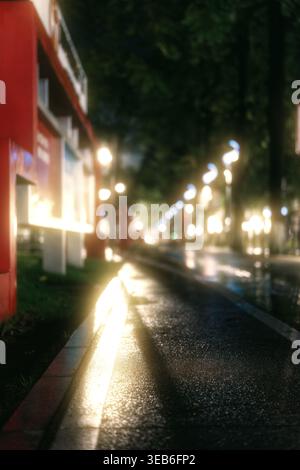 Regnerische Nachtstraße in der Stadt mit unscharfen Lichtern und Reflektionen auf nassem Gehweg Stockfoto