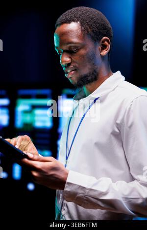 afroamerikanischer Administrator verwendet Laptop, um den Energieverbrauch für die einzelnen Server-Rack-Teile zu überprüfen. Professionelle Mitarbeiter stellen sicher, dass die elektronischen Temperatursensoren für Rechenzentren in einwandfreiem Betriebszustand sind Stockfoto