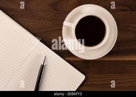 Top-down-Nahaufnahme der Kaffeetasse mit offenem leerem Notizbuch auf Holztisch Stockfoto