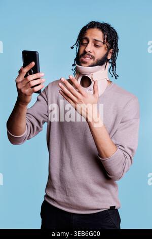 Arabischer Patient mit Halsband im Online-Gespräch mit Arzt auf Smartphone. Mann mit Nackenbügel spricht mit Hausarzt auf Smartphone über Trauma Stockfoto