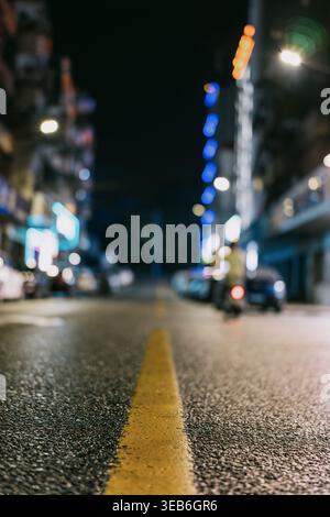Nächtliche urbane Straßenszene mit verschwommenen Stadtlichtern, gelber Straßenlinie im Vordergrund, Stockfoto