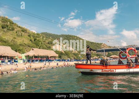 Santa marta, kolumbien - Noviembre 02, 2025 Touristen entspannen und schwimmen an einem pulsierenden karibikstrand, mit einem Bootsbetreiber und einer Seilrutsche, die abo führt Stockfoto