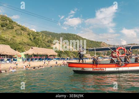 Santa marta, kolumbien - Noviembre 02, 2025 Urlauber, die sich an einem Sandstrand entspannen und im Meer schwimmen, ein Boot mit Passagieren und eine Person mit Reißverschlüssen Stockfoto