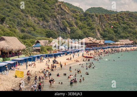 Santa marta, kolumbien - Noviembre 02, 2025 Touristen entspannen und schwimmen am playa blanca Beach, santa marta, kolumbien, mit strohgedeckten Hütten und Lu Stockfoto