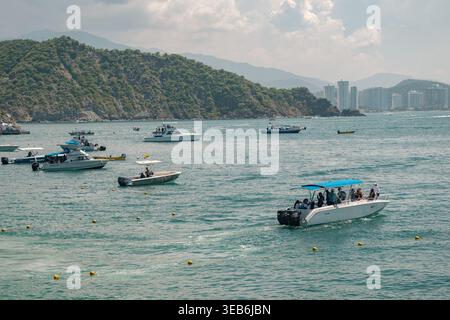 Santa marta, kolumbien - Noviembre 02, 2025 Personen genießen eine Bootsfahrt in der karibik, mit einer Küstenstadt und grünen Bergen, die ein pulsierendes Leben schaffen Stockfoto