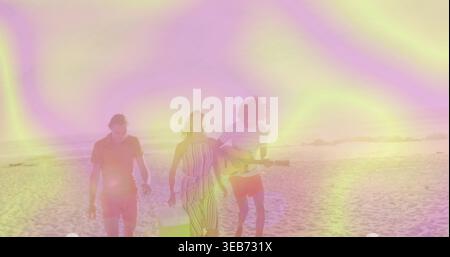 Spazierendes Trio mit Frau in gestreiftem Sommerkleid mit weißer Tasche und Mann, der am Strand Gitarre spielt Stockfoto