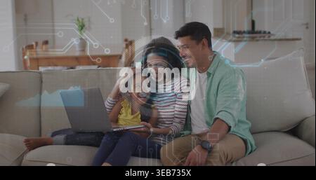 Lächelnde Familie sitzt zu Hause auf hellbeigem Sofa, Kind hält Tablet mit digitalem HUD Stockfoto