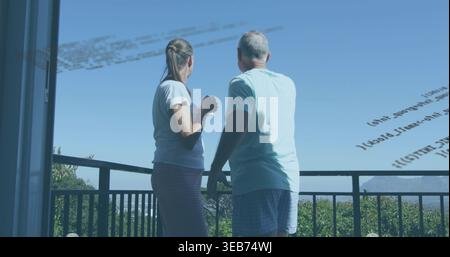 Stehende Seniorenpaare in Freizeitkleidung, die Hügel auf dem Balkon mit Becher und Code-Reflexion betrachten Stockfoto