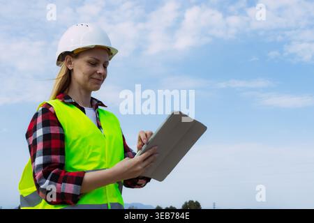 Architektin oder Vorgesetzte trägt eine Reflektorweste und einen Schutzhelm. Arbeiten mit einem digitalen Tablet, um Blueprints zu überprüfen. Aufgaben verwalten. Und für Profis sorgen Stockfoto