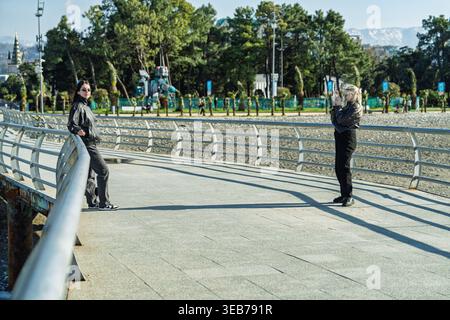 Batumi, georgia 21. april 2026: Junge Frauen genießen Besichtigungs- und Fotografieausflüge entlang der Promenade in batumi, georgia, mit Bäumen und Bergen Stockfoto