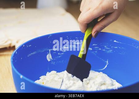 Nahaufnahme einer blauen Rührschüssel mit weißer Schlagsahne und Silikonspachtel, bereit zum Dekorieren oder Backen von Kuchen. Stockfoto