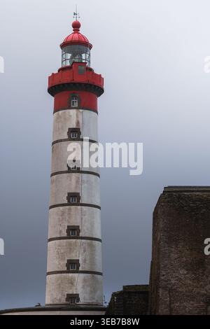 Blick auf den Leuchtturm von Pointe Saint-Mathieu mit seinem roten Laternenraum und dem weißen Turm neben alten Steinmauern unter einem bewölkten Himmel in Ploug Stockfoto