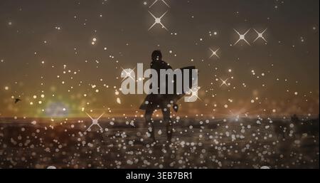 Stehender Mann mittleren Alters im Neoprenanzug, Surfbrett auf nassem Sand bei Sonnenuntergang, mit Sternenbokeh Stockfoto
