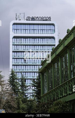 Batumi, georgia 21. april 2026: batumi, georgia, Stadtbild mit einem zeitgenössischen Wolkenkratzer mit Glasfassade im Kontrast zu einem traditionellen Grün Stockfoto