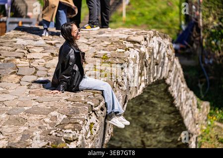 Batumi, georgia 21 april 2026: Junge Frau in lässiger Sommerkleidung sitzt auf einer alten Bogenbrücke in batumi, georgia, und genießt eine ruhige Stadt Stockfoto