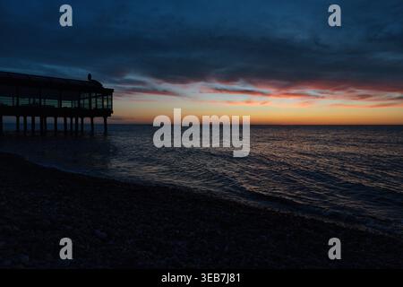 Batumi, georgia 21. april 2026: Restaurant auf Stelzen über dem schwarzen Meer in batumi, das in einem dramatischen orange-blauen Sonnenuntergang leuchtet, der sich auf Kieselstein bea spiegelt Stockfoto