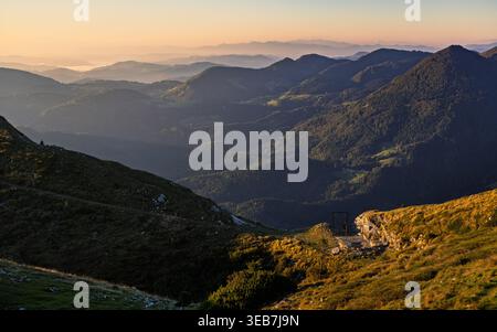 Blick auf sanfte Bergkämme und bewaldete Hügel unter einem sanften goldenen Sonnenaufgang mit Nebel in den Tälern Sorica, Skofja Loka, Slowenien. Stockfoto