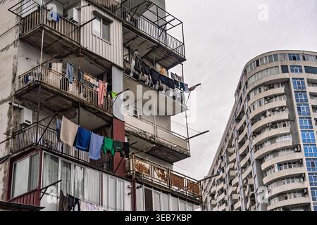 Batumi, georgia 21. april 2026: Städtische Wohngebäude mit Wäschetrocknung auf verwitterten Balkonen neben einem eleganten, geschwungenen Hochhaus in batumi, Stockfoto