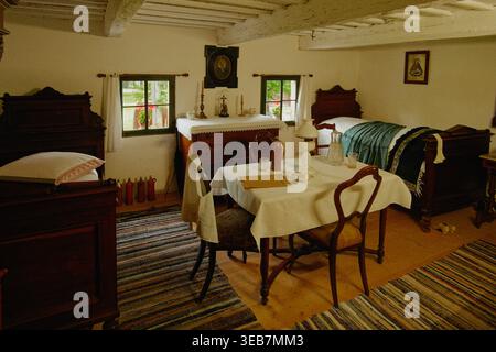 Die Warme Morgenbeleuchtung Unterstreicht Traditionelle Bettwäsche Und Holzmöbel Im Ländlichen Tschechischen Salon Stockfoto
