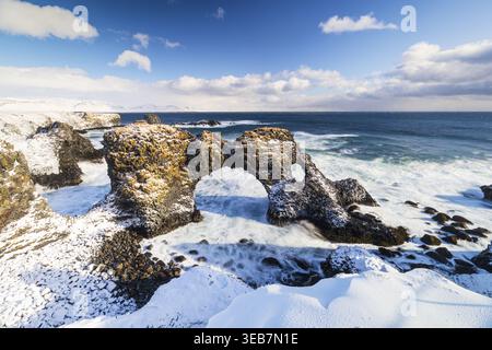Blick auf die Küste der Halbinsel Snaefellsnes mit einem schneebedeckten Natursteinbogen gegen das blaue Meer in Eyja- og Miklaholtshr, Island. Stockfoto