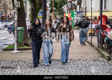 Batumi, georgia 21. april 2026: Drei junge Freunde schlendern und plaudern auf einer kopfsteingepflasterten batumi-Straße, erkunden die Stadt und lachen Stockfoto
