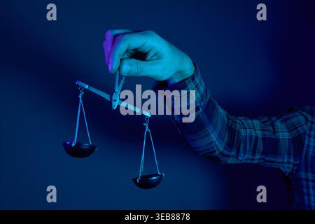 Konzeptuelle Kunst einer Hand mit kleinen Skalen im blauen Neonlicht. Metapher für Gerechtigkeit, Ausgewogenheit, Entscheidungsfindung und Rechtssystem. Stockfoto